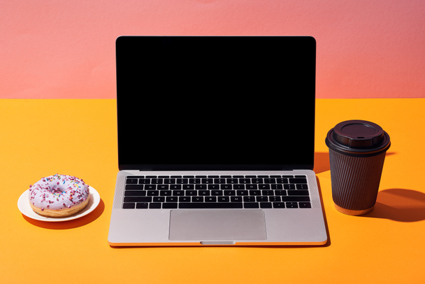 laptop met leeg scherm in de buurt van donut en papier koffiekopje op gele achtergrond van de oppervlakte en roze - Foto, afbeelding