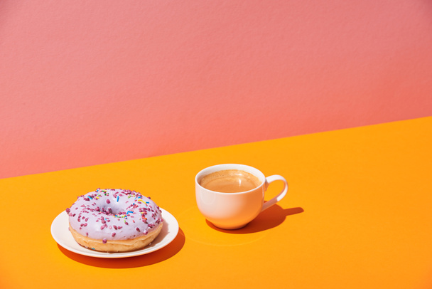 tasty donut with saucer and coffee cup on yellow surface and pink background - Фото, изображение