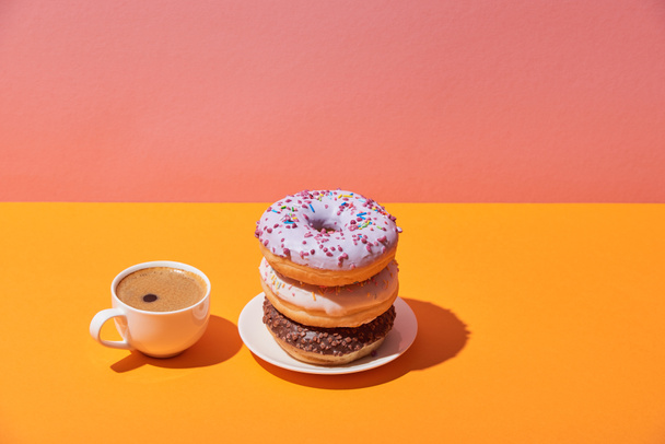 tasty donuts on saucer and coffe cup on yellow desk and pink background - Fotó, kép