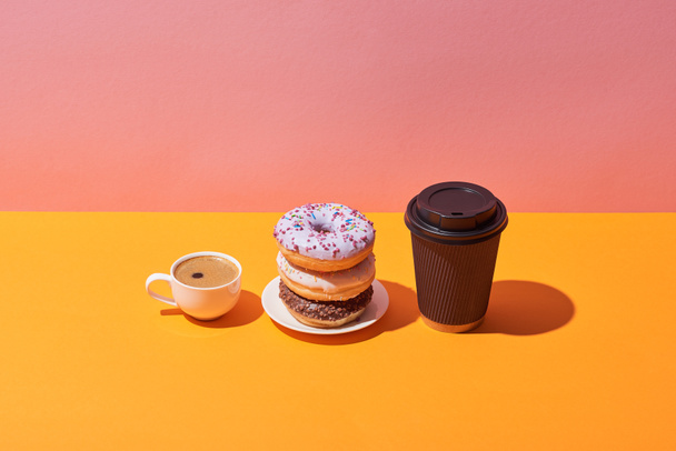 sabrosos donuts en platillo y tazas de café sobre escritorio amarillo y fondo rosa
 - Foto, Imagen