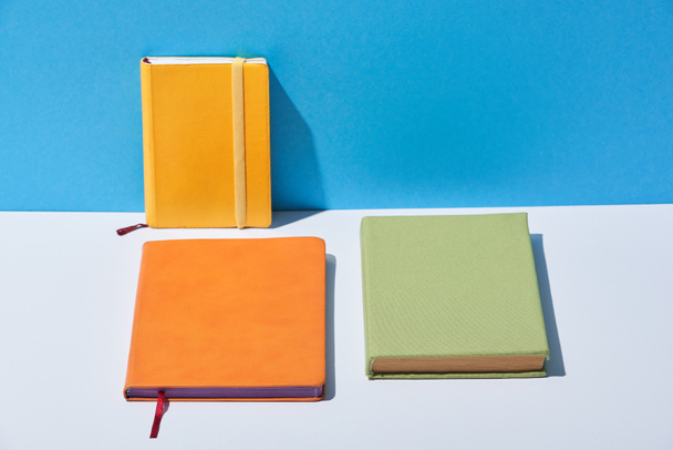 multicolored notebooks on white desk and blue background - Fotoğraf, Görsel