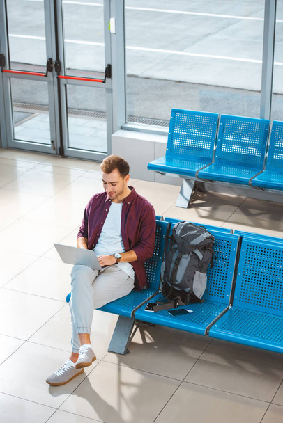 overhead view of handsome man using laptop while sitting in waiting hall - Foto, Bild