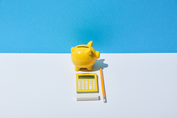 calculadora, alcancía, borrador y lápiz sobre escritorio blanco y fondo azul
 - Foto, Imagen