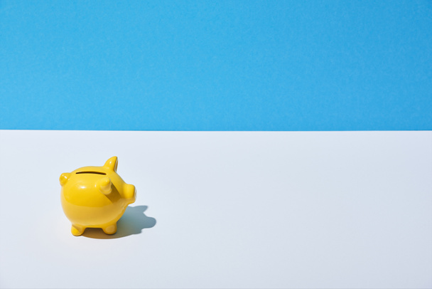 keltainen säästöpossu valkoisella pöydällä ja sininen tausta
 - Valokuva, kuva