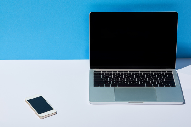 laptop with blank screen and smartphone on white desk and blue background - Foto, Bild