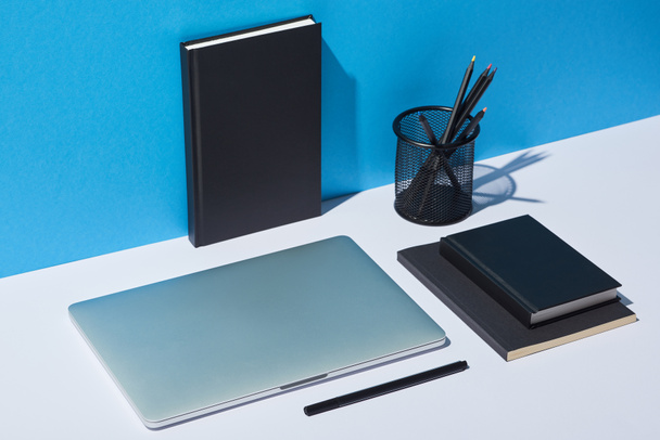 laptop, pencil holder and notebooks on white desk and blue background - Фото, зображення