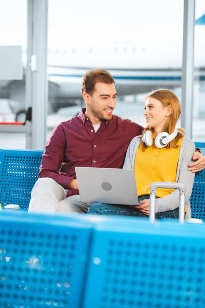 couple souriant se regardant près d'un ordinateur portable à l'aéroport
 - Photo, image