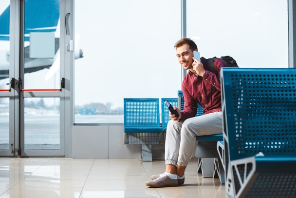 vrolijke man praten over smartphone zittend in de vertreklounge - Foto, afbeelding