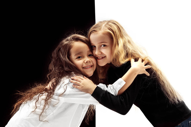 The portrait of two hugging embracing happy girls on a white and black studio background. Human emotions concept. Comparison. The childhood, smile, happiness, joy, kid, friendship concept - Fotografie, Obrázek