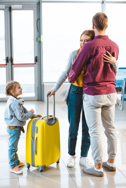 lindo niño sosteniendo oso de peluche y mirando a mamá y papá abrazándose en el aeropuerto
  - Foto, Imagen