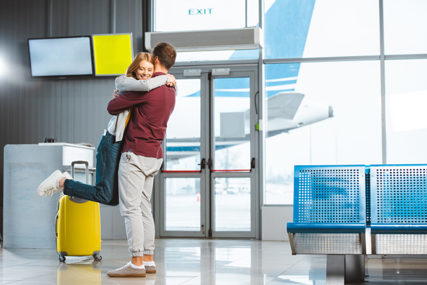 beautiful woman hugging boyfriend in waiting hall near baggage  - Fotografie, Obrázek