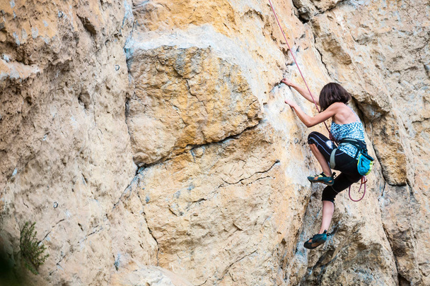 A rapariga sobe a rocha. O alpinista está treinando para escalar a rocha. Um atleta forte supera uma rota de escalada difícil. Passatempo extremo. Uma mulher entra para praticar desporto na natureza. Terreno rochoso natural
. - Foto, Imagem