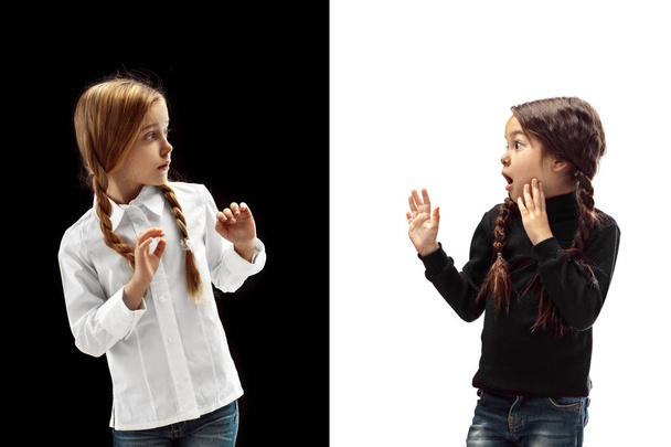 The portrait of two frightened, afraid, scared girls on a white and black studio background. Human emotions concept. Comparison. The childhood, smile, happiness, joy, kid, friendship concept - Fotoğraf, Görsel