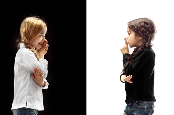 Secret, gossip concept. Young girls whispering a secret behind her hand isolated on white and black studio background. Young emotional girl. Human emotions, facial expression concept. - Photo, image