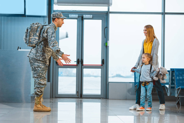 dad in military uniform standing with opened arms near wife and daughter in airport  - Fotó, kép