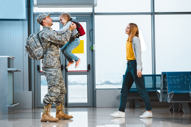 happy father in military uniform holding in arms cute daughter near wife in airport  - Фото, изображение