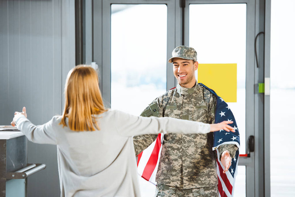 selective focus of happy boyfriend in military uniform looking at girlfriend with opened arms  in airport  - 写真・画像