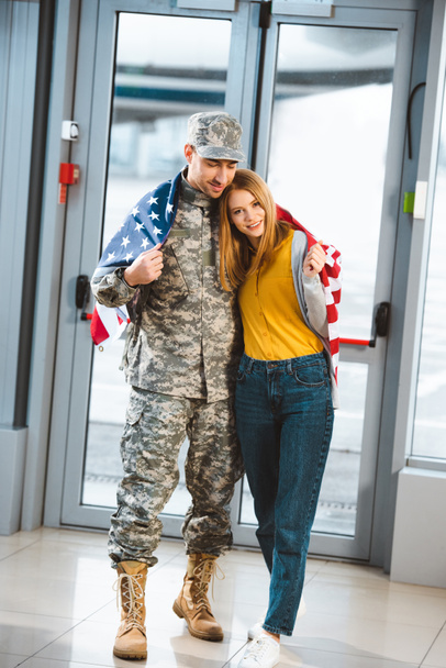 happy veteran in military uniform standing with girlfriend and holding american flag in airport  - Foto, Imagem