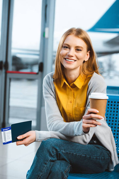 attraktive Frau lächelt, während sie Einwegbecher im Flughafen in der Hand hält  - Foto, Bild