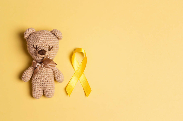 Children's toy with a Childhood Cancer Awareness Yellow Ribbon on yellow background. Childhood Cancer Day February, 15. - Fotoğraf, Görsel