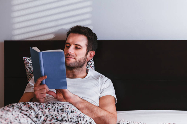 Nuori mies lukee kirjaa sängyssä - Valokuva, kuva