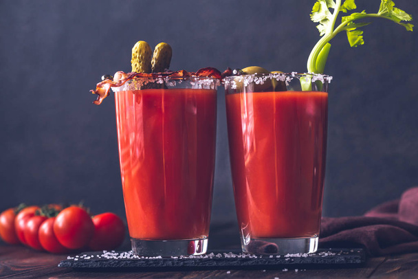 Two glasses of Bloody Mary garnished with gherkins, fried bacon strips, green olives and celery stalk - Foto, Imagem