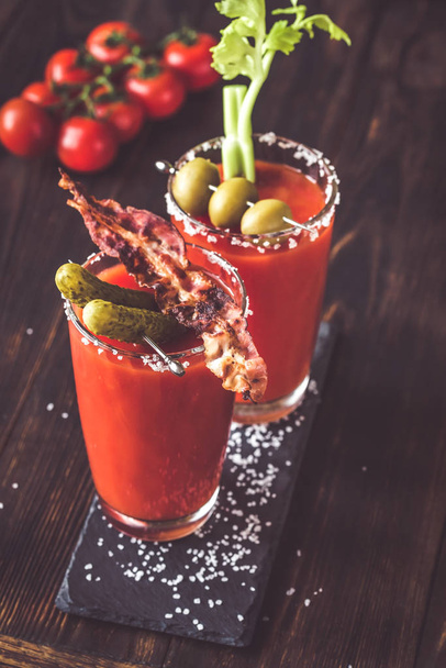 Two glasses of Bloody Mary garnished with gherkins, fried bacon strips, green olives and celery stalk - Photo, Image