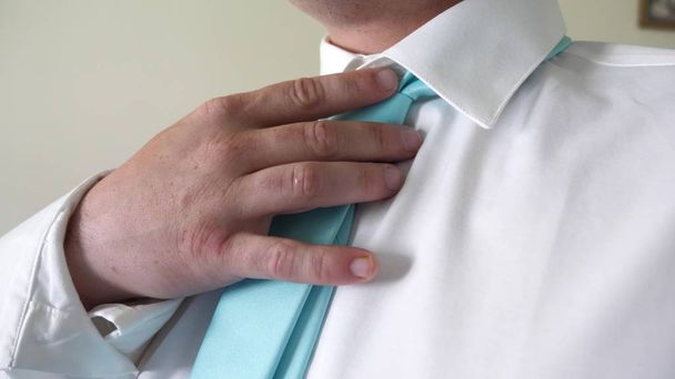 Businessman man puts on blue tie with his hands to white shirt in morning going to work. Concept of business employee. Dress code. Close-up - Zdjęcie, obraz