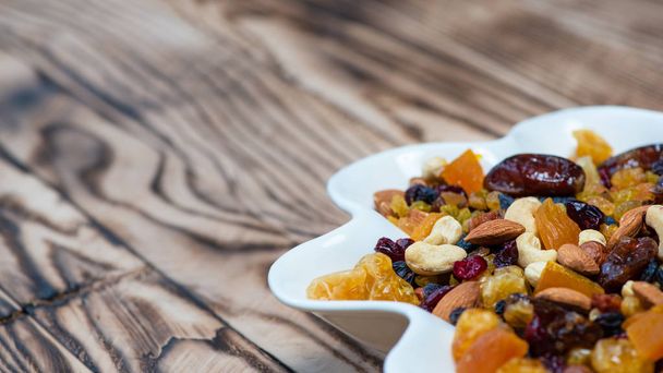 Dried fruits in white plate on wooden table. Mix of different varieties of nuts and berries, vitamins. With copy space for text - 写真・画像