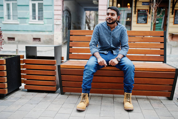 Stylish indian beard model man in casual clothes posed outdoor, sitting on bench at street of India. - Photo, Image