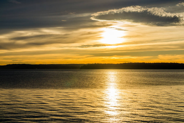 Blick auf den Sonnenuntergang auf dem Puget Sound, der einen dunkelgoldenen Schein erzeugt. - Foto, Bild