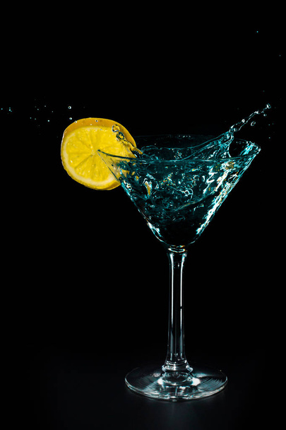 Splash ποτό κοκτέιλ μπλε του νερού στο ποτήρι με λεμόνι απομονώνονται σε μαύρο φόντο - Φωτογραφία, εικόνα