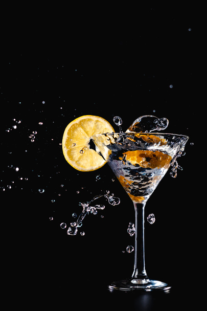 Bebida de agua de cóctel salpicada en el vaso con limón Aislado sobre fondo negro
 - Foto, Imagen