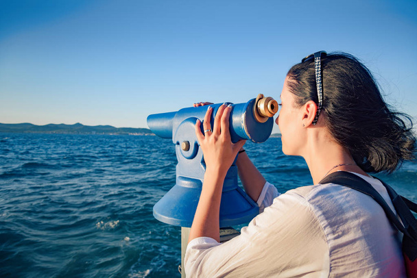 junge Frau blickt im Teleskop oder Fernglas auf das Meer. - Foto, Bild