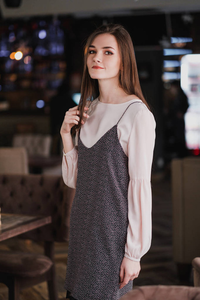 Portrait of a young girl with long hair on the background of luminous signs in the interior of a cafe or restaurant. Black dress and blouse, elegant and attractive. - Foto, Imagen
