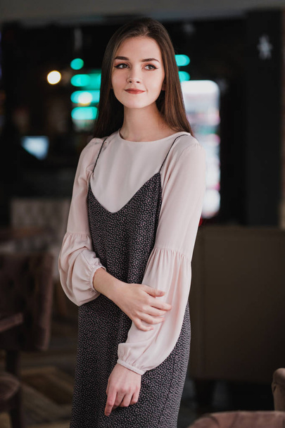 Portrait of a young girl with long hair on the background of luminous signs in the interior of a cafe or restaurant. Black dress and blouse, elegant and attractive. - Fotoğraf, Görsel