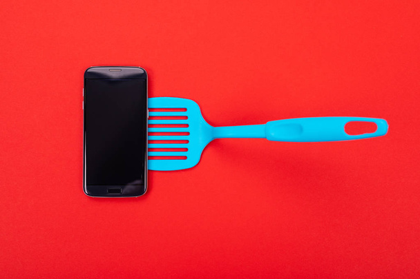 Top view of smart phone as part of cooking equipment in kitchen isolated on red background - Photo, Image