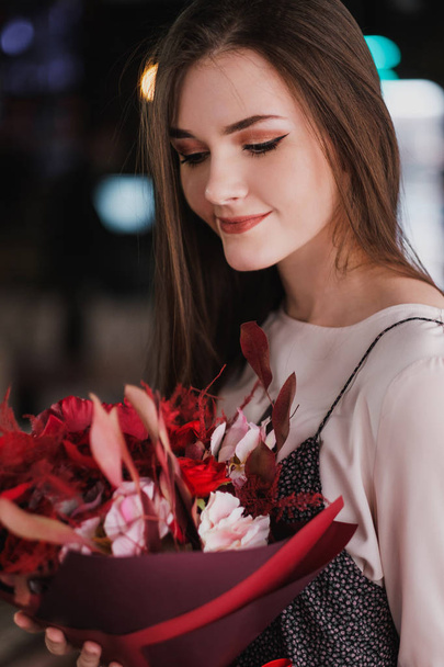 The girl is sitting in a cafe with a bouquet of red flowers, peonies, roses and chrysanthemums. - Valokuva, kuva