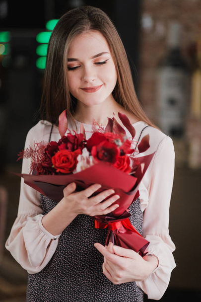 Дівчина сидить в кафе з букетом червоних квітів, півоній, троянд і хризантем
. - Фото, зображення