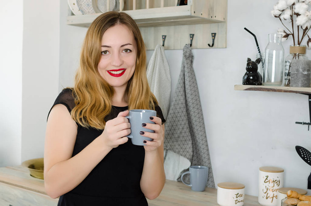 Portrait of smiling young woman with cup against kitchen interior background. - Фото, изображение