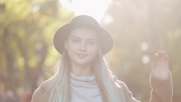 Amazing girl in a romantic look, with black hat walking down the park alley, looking into the camera and gives amazing smile. Park settings, trees, fallen leaves on the background - Footage, Video
