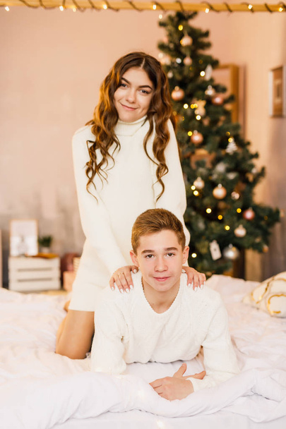 young beautiful couple are sitting on the bed on the background of the Christmas tree and smiling - Photo, Image