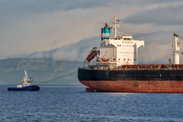 Фотографія вантажного корабля, що входить у природу буксирується буксирним човном
 - Фото, зображення