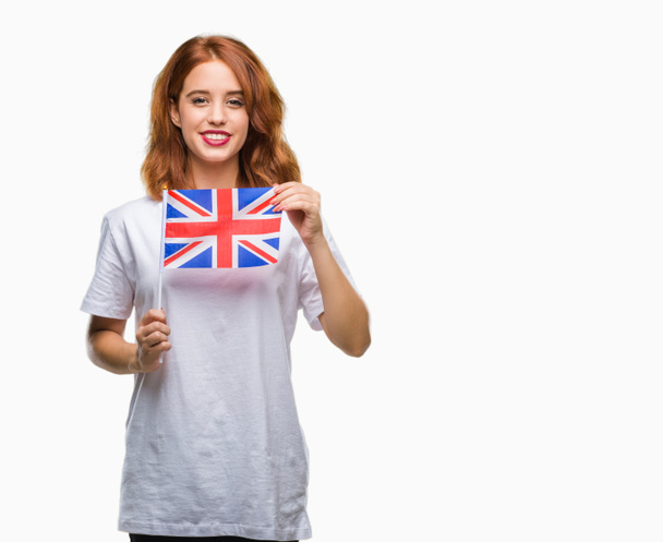 Jovem bela mulher segurando bandeira do reino unido sobre fundo isolado com um rosto feliz de pé e sorrindo com um sorriso confiante mostrando dentes
 - Foto, Imagem