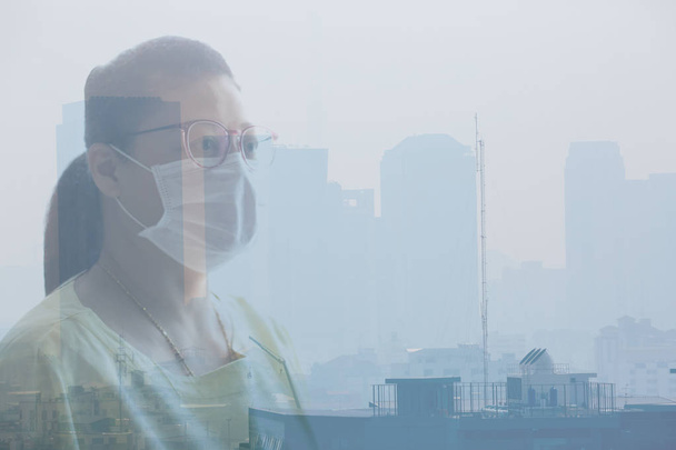 Woman wearing face mask because of air pollution in the Bangkok. Woman wearing face mask with background of Office building under smog in Din Daeng District, Bangkok Thailand. Smog is a kind of air pollution. Bangkok City in the air pollution. - Zdjęcie, obraz