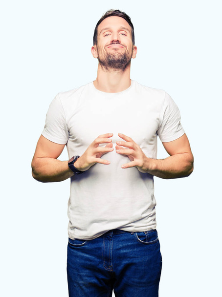Pohledný muž nosí ležérní bílé tričko ruce dohromady a prsty palce, usmíval se uvolněně a vesele. Úspěch a optimistické - Fotografie, Obrázek