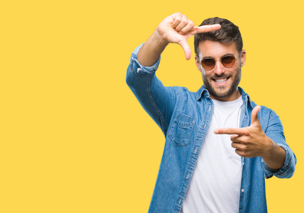 Young handsome man wearing sunglasses over isolated background smiling making frame with hands and fingers with happy face. Creativity and photography concept. - Photo, Image