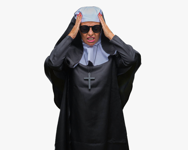 Femme religieuse catholique âgée d'âge moyen portant des lunettes de soleil sur fond isolé souffrant de maux de tête désespérés et stressés parce que la douleur et la migraine. Mains sur la tête
. - Photo, image