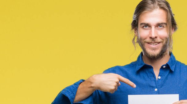 Young handsome man with long hair over isolated background holding blank paper with surprise face pointing finger to himself - Photo, Image