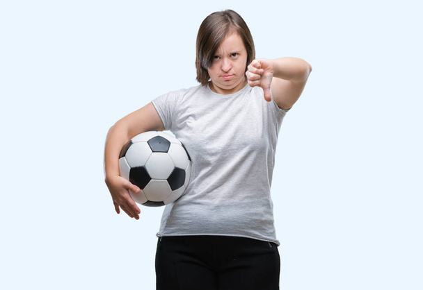 Молодая взрослая женщина с синдромом Дауна держит футбольный мяч на изолированном фоне с сердитым лицом, негативный знак показывает неприязнь с опущенными пальцами, отвержение концепции
 - Фото, изображение